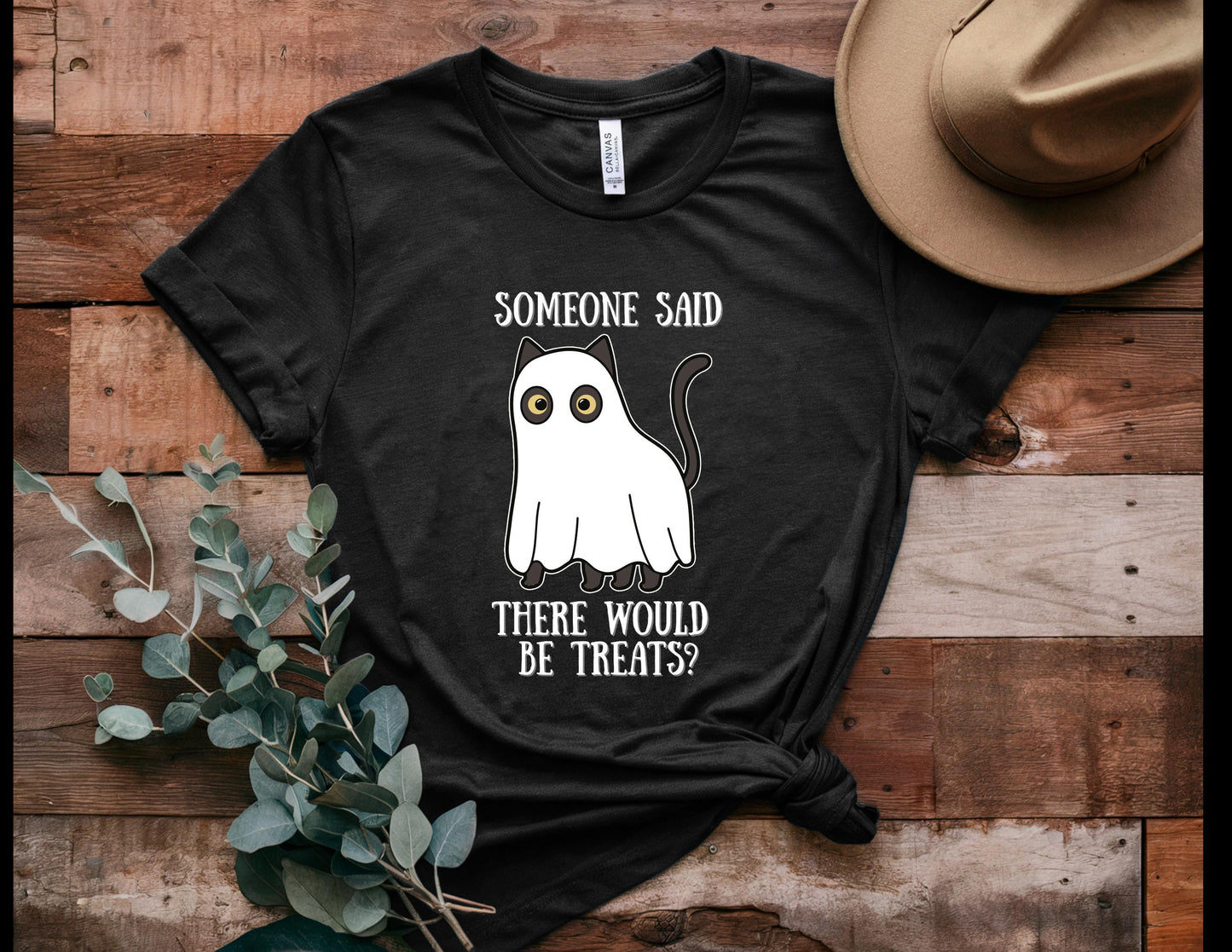 Black t-shirt with ghost and text design on a wooden surface with a hat and plant.