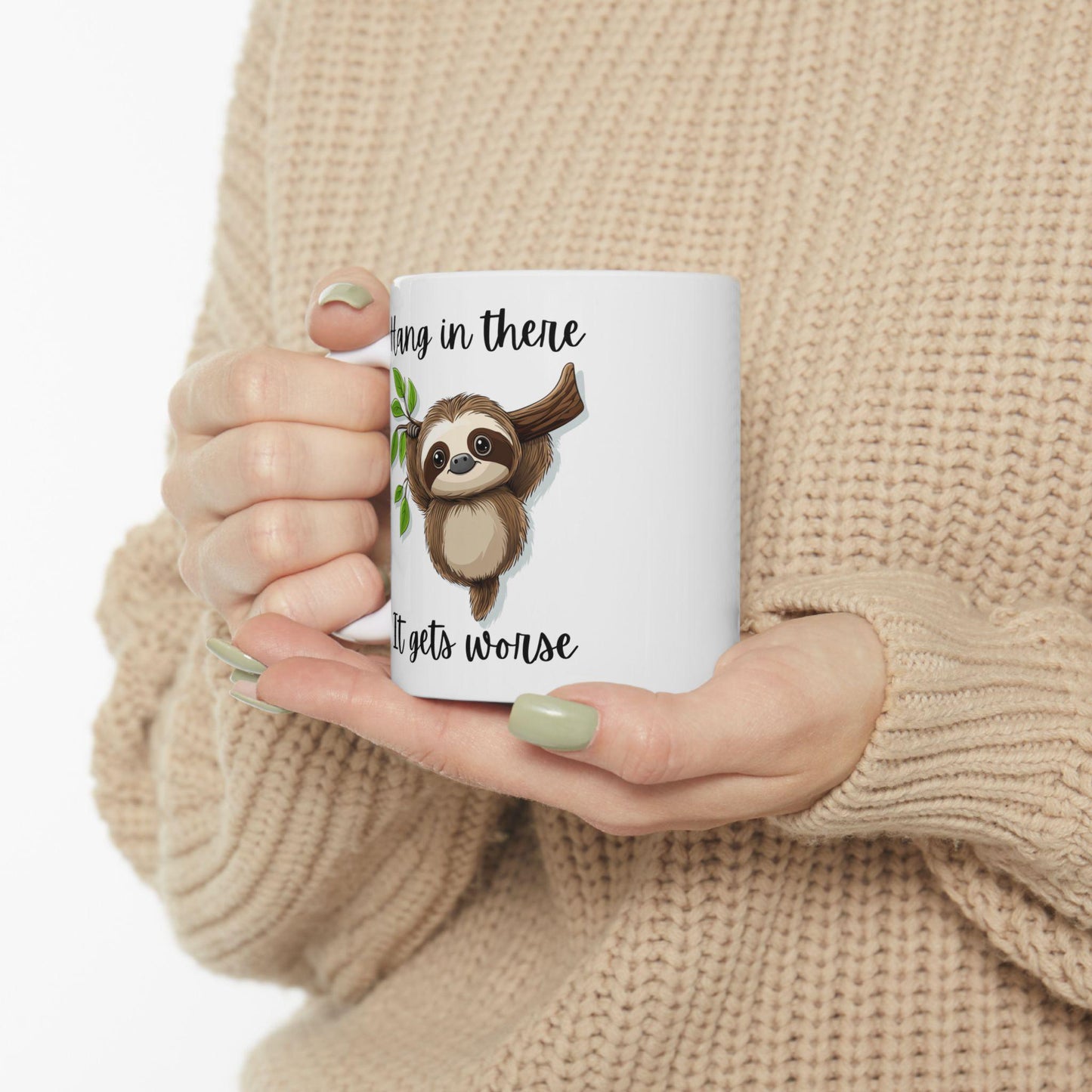 Person holding a mug with a sloth design and text, wearing a beige sweater.