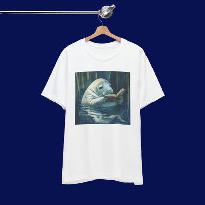 White t-shirt with a graphic of a manatee reading a book in water, hanging on a wooden hanger against a white background.