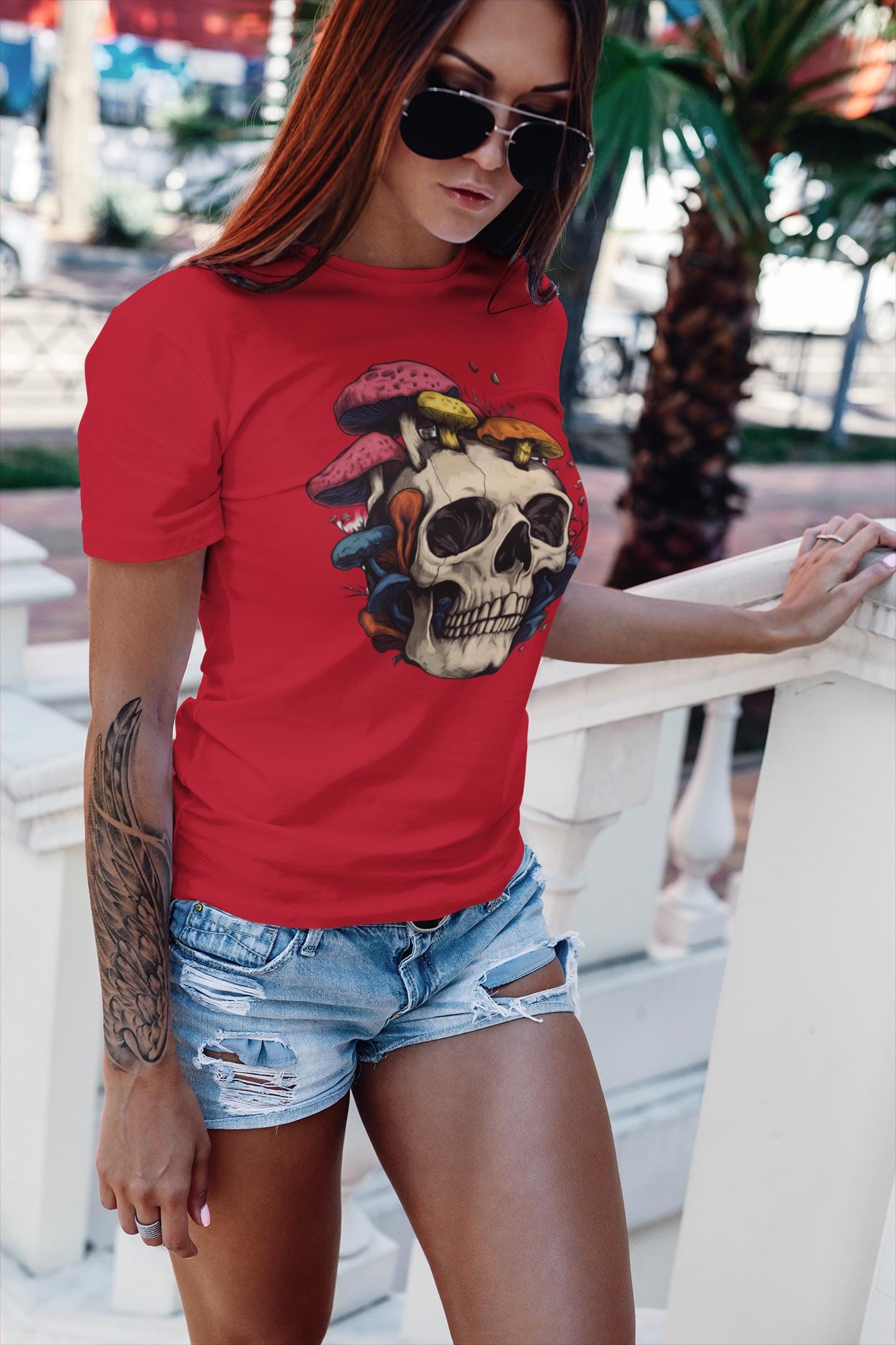 Woman wearing a red t-shirt with a skull and mushroom design, standing outdoors.