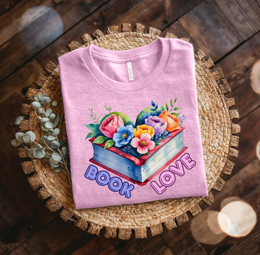 Folded pink t-shirt with floral design and 'Book Love' text on a woven mat.