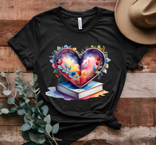 Black t-shirt with a colorful heart design on a wooden surface with a hat and plant.