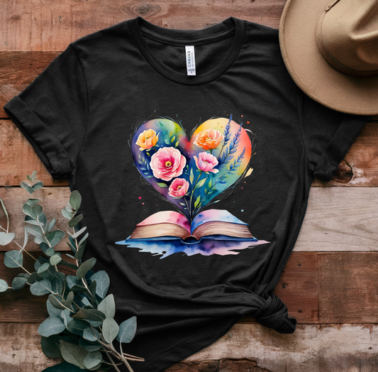 Black t-shirt with a colorful heart design featuring flowers and an open book on a wooden surface.