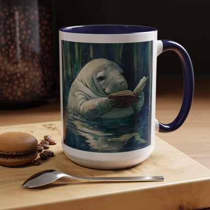 Mug with a design of a manatee reading a book on a wooden surface with coffee beans and a macaron.