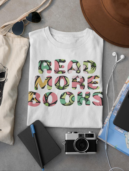 White t-shirt with 'READ MORE BOOKS' text on a gray surface with accessories.