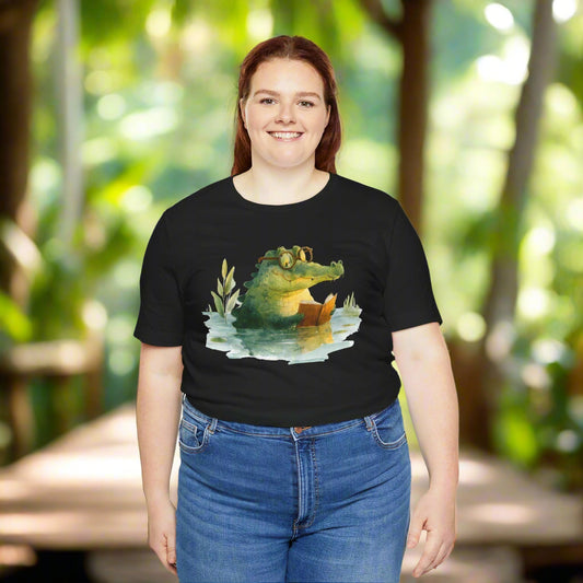 Person wearing a black t-shirt with a graphic of an alligator reading a book.