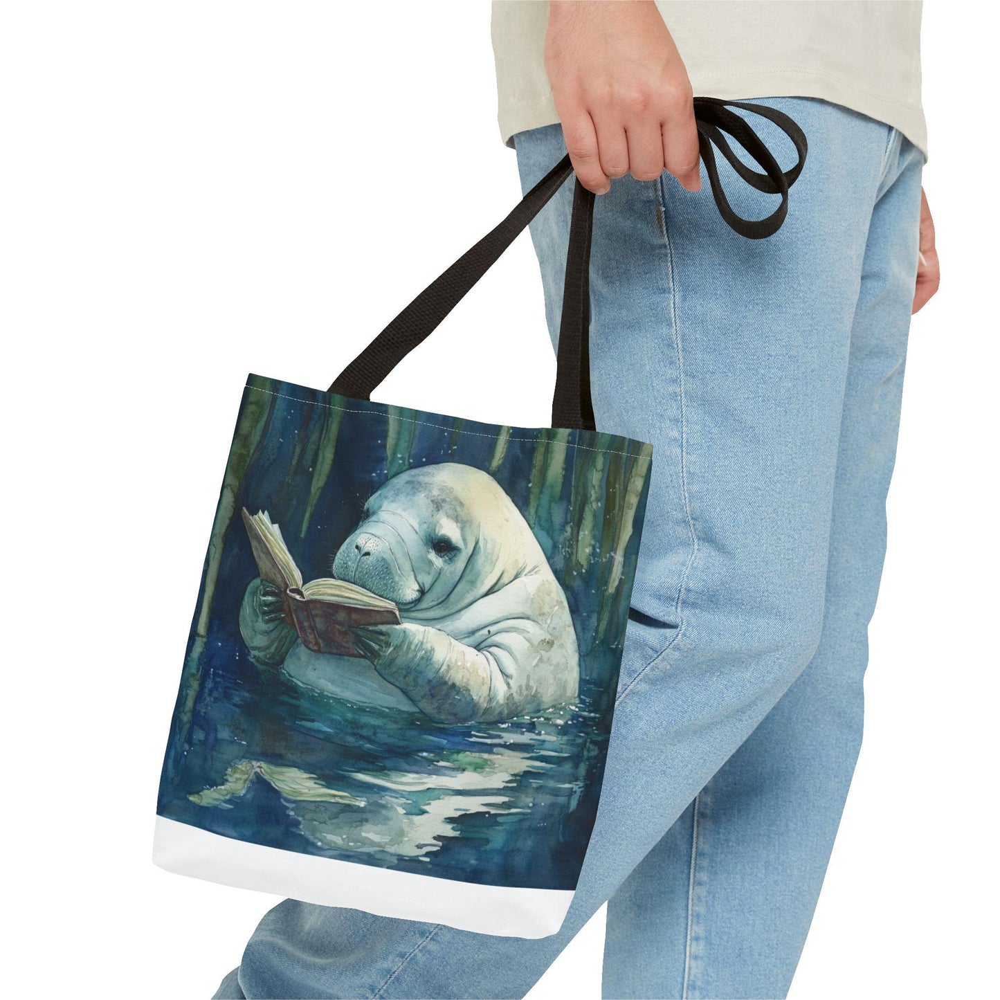 Tote bag with a design of a manatee reading a book, held by a person wearing jeans.