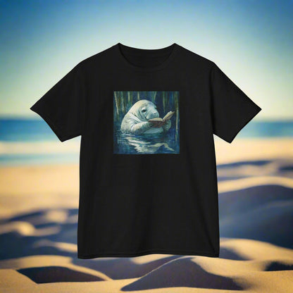 Black t-shirt with a manatee reading a book graphic on a beach background