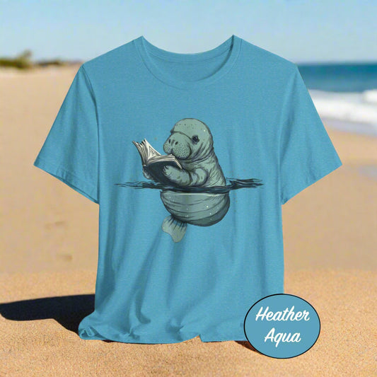 Blue t-shirt with a manatee reading a book design on a light beach background