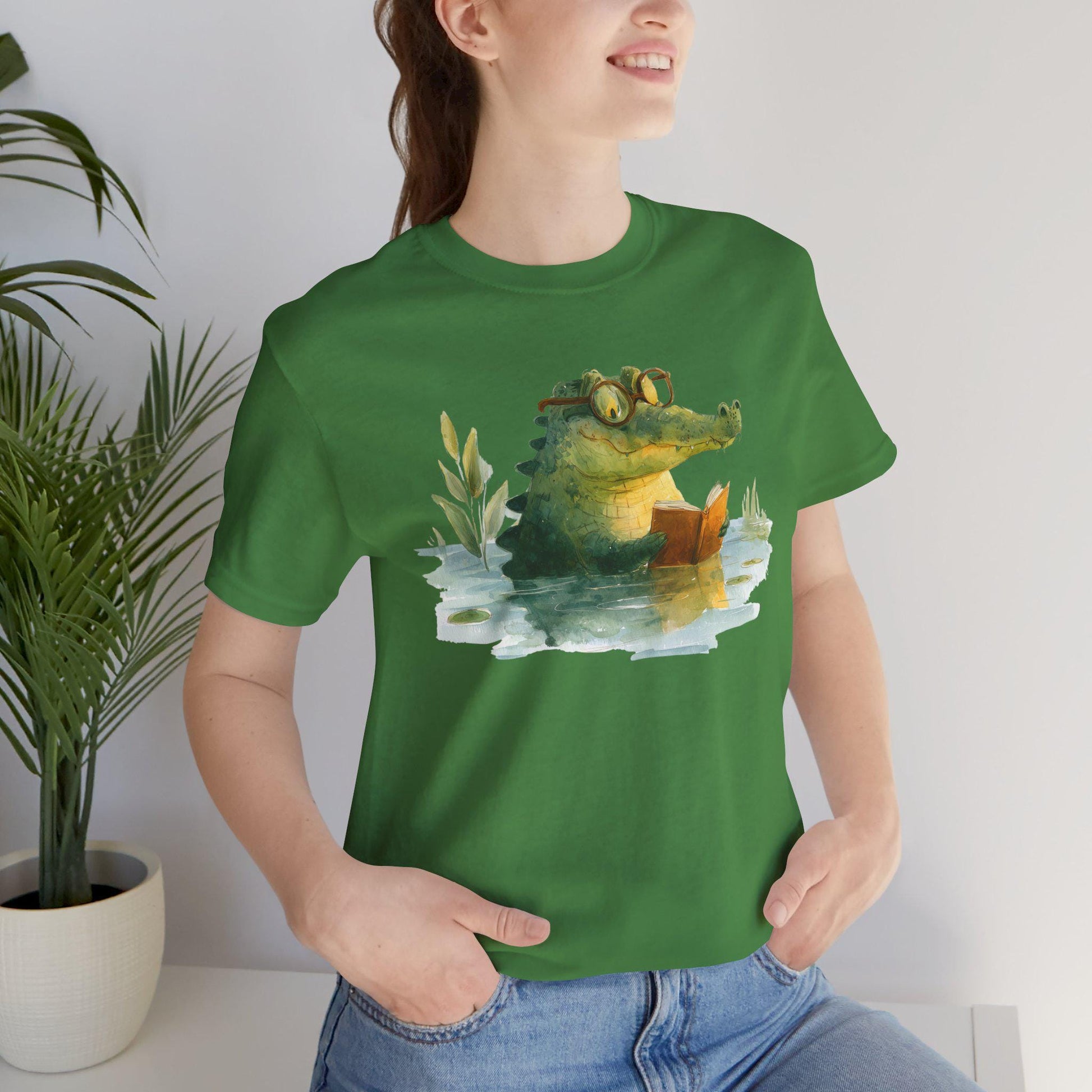 Person wearing a green t-shirt with a crocodile graphic, standing indoors next to a plant.