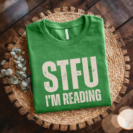 Green t-shirt with 'STFU I'm Reading' text on a woven mat