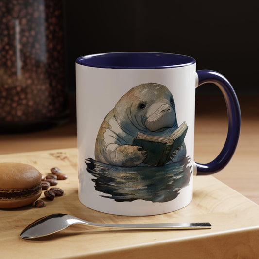 Mug with a manatee reading a book design on a table with coffee beans and a spoon.