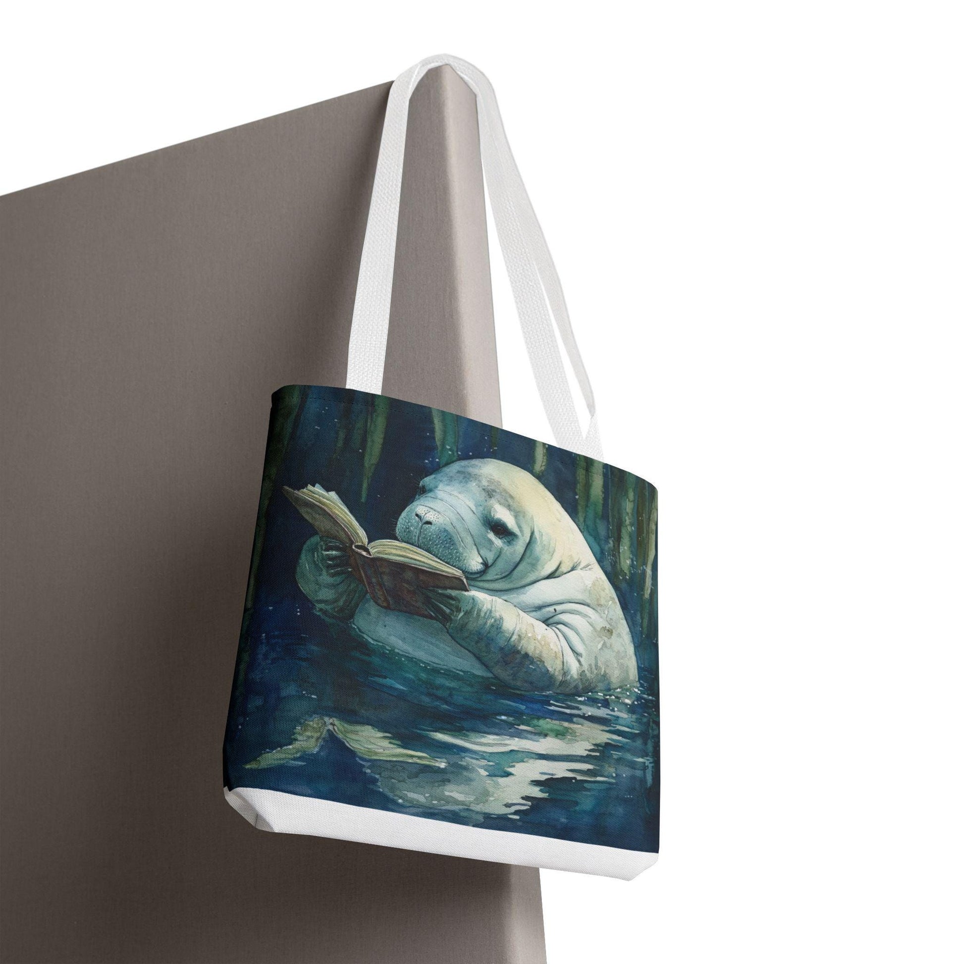 Tote bag with a design of a manatee reading a book on a white background