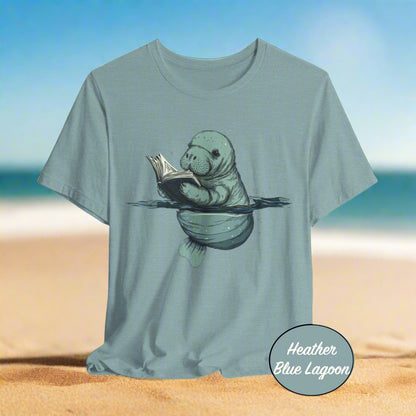 Heather blue t-shirt with a manatee reading a book graphic on a light gray background.