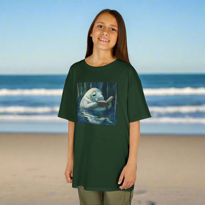 Child wearing a green t-shirt with a graphic of a manatee reading a book on a beach background