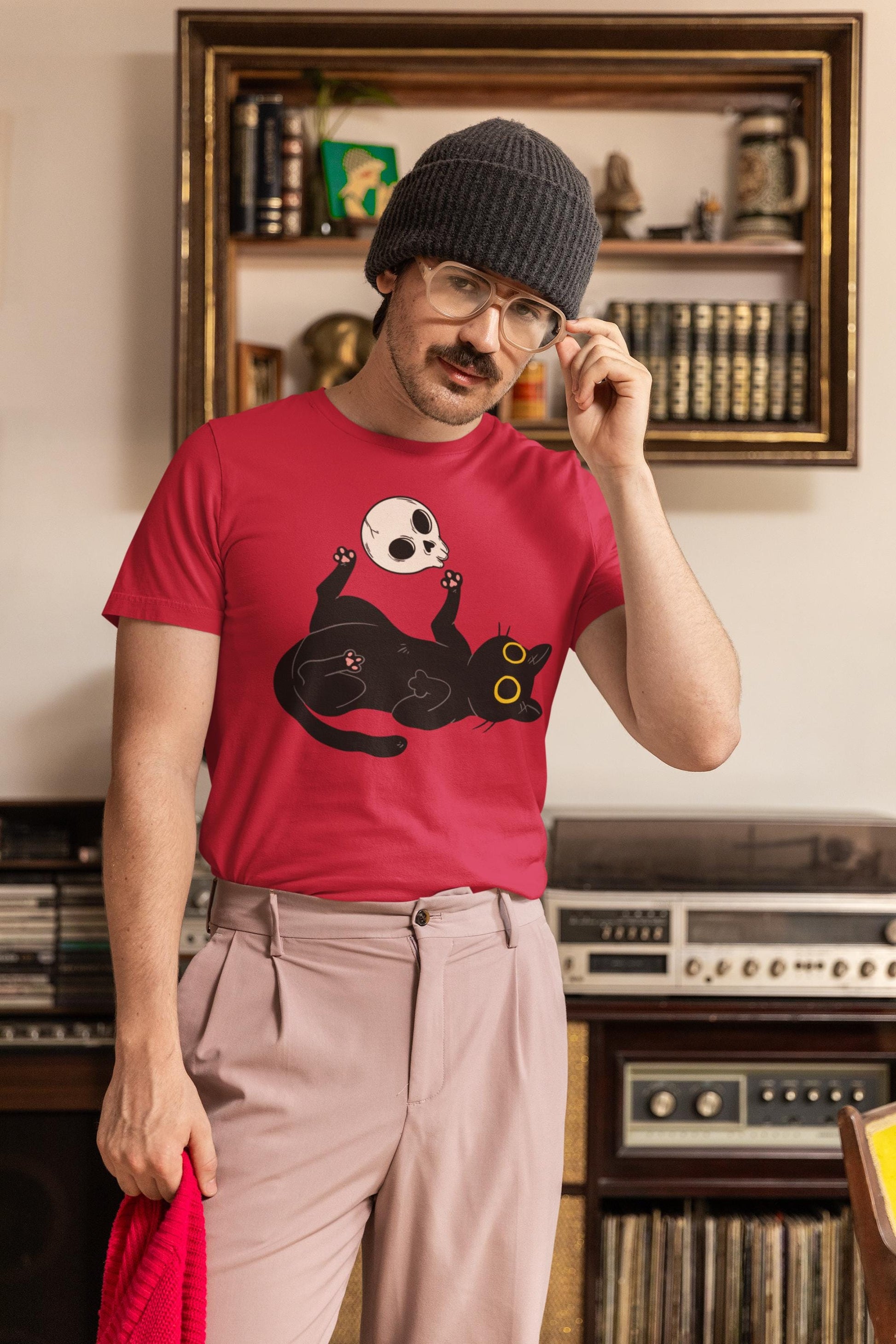 Man wearing a red t-shirt with a black cat design, standing in a room with vintage stereo equipment.