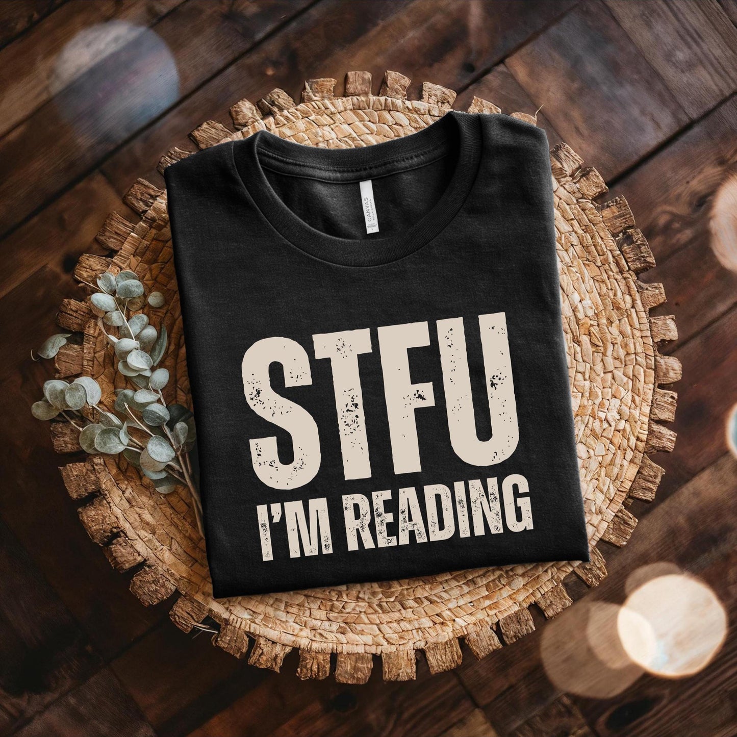 Black t-shirt with 'STFU I'm Reading' text on a woven mat.