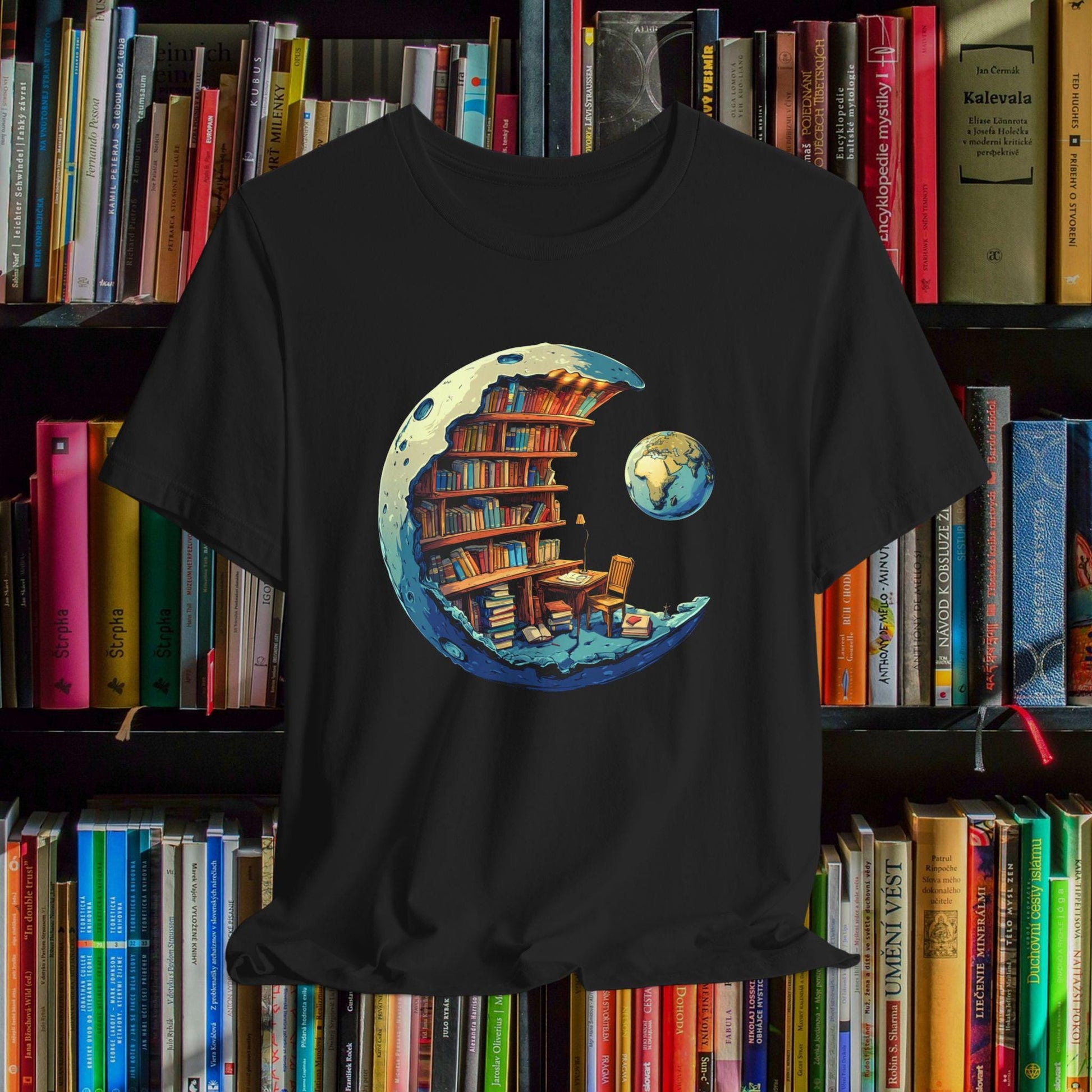 Black t-shirt with a crescent moon design featuring books and a desk, placed on a bookshelf.