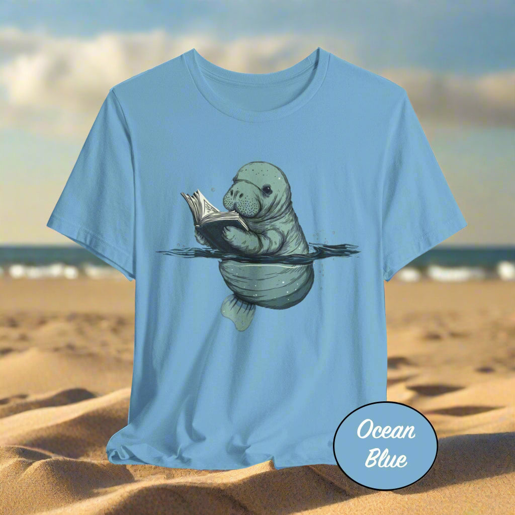 Blue t-shirt with a manatee reading a book graphic on a light gray background