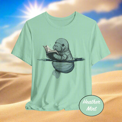 Mint green t-shirt with a graphic of a manatee reading a book on a light gray background.