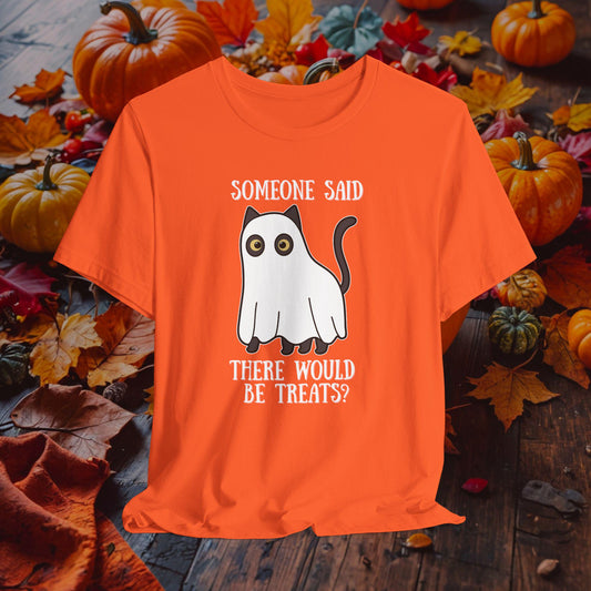Orange t-shirt with a Halloween-themed graphic of a ghost and text, placed on a wooden surface with pumpkins and leaves.
