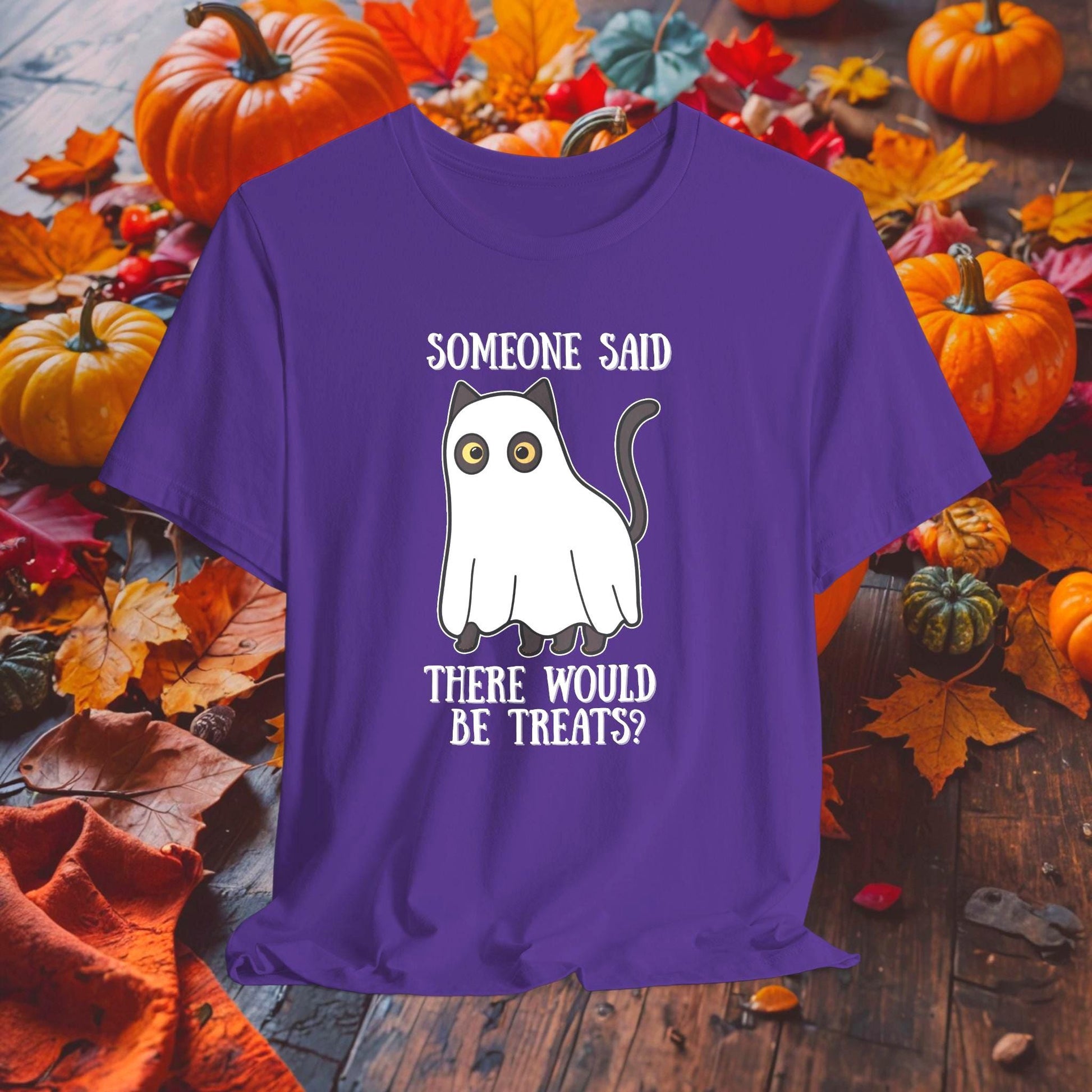 Purple t-shirt with a ghost graphic and text on a wooden surface with pumpkins and leaves.