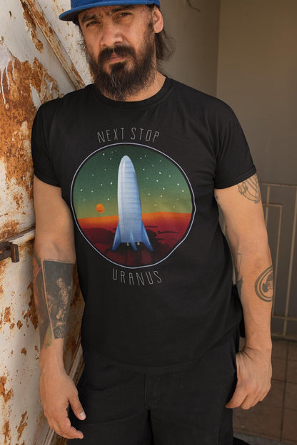Person wearing a black t-shirt with a graphic design and text, standing against a wall.